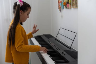 Beyaz üzerinde elektrikli piyano çalan tatlı, ciddi, küçük bir kız.