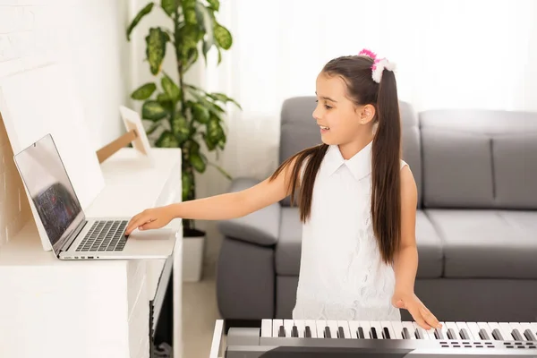 Домашняя школа маленькая девочка, изучающая фортепиано с помощью компьютера, подключенного к онлайн-классу музыки школьным учителем. Новый нормальный образ жизни и образование, студент учится дома. — стоковое фото