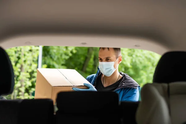 Man by the car. Guy in a delivery uniform. Man in a medical mask. Coronavirus concept.