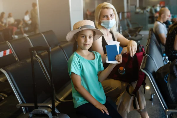 Turista madre e hija con máscara protectora de higiene en rostros sentados en la terminal del aeropuerto. Idea para la seguridad del nuevo viajero normal y el distanciamiento social. —  Fotos de Stock