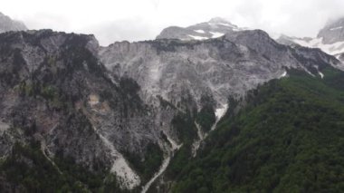 Arnavutluk 'un Theth kentinde rüzgarlı bir günde Alp dağlarının yamacında yeşil çimenli çayır