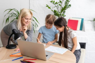 Anne ve iki kız evde ödev yapıyor ve kitap okuyor.