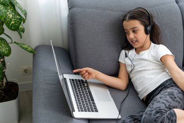 Evde dizüstü bilgisayarı olan küçük bir kız çocuğu. Mutlu küçük çocuk bilgisayar kullanarak içeride oynuyor..