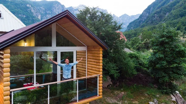 Przystojny młody człowiek stoi na balkonie wiejskiego mieszkania odwraca wzrok z uśmiechem na twarzy na tle gór. Odpocznij w górach — Zdjęcie stockowe