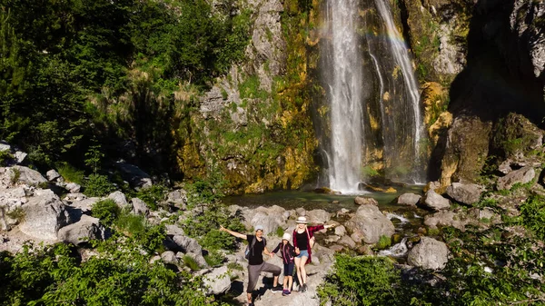Famille de trois personnes relaxant et bénéficiant d'une belle vue sur la cascade lors d'une randonnée dans les montagnes — Photo