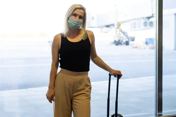 Femme portant un masque pour prévenir le virus avec des bagages à l'aéroport international. Protection contre le coronavirus — Photo