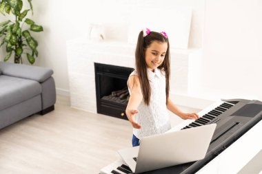 Piyano çalan küçük kız çocuğu. Bilgisayardan öğretmenle çevrimiçi müzik dersi