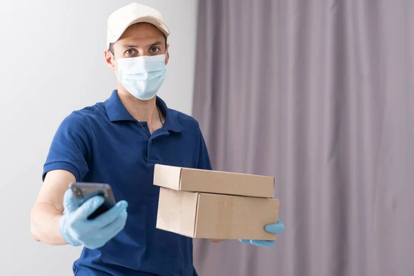 Доставщик в защитной маске и перчатках держит коробку с продуктами — стоковое фото