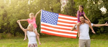 Amerikan bayrağı taşıyan ebeveynler ve çocuklar renkli bir uçurtmayla oynuyorlar. Anne, baba ve küçük kızları sisli bir günde 4 Temmuz 'u birlikte kutluyorlar. ABD 'nin Bağımsızlık Günü konsepti.