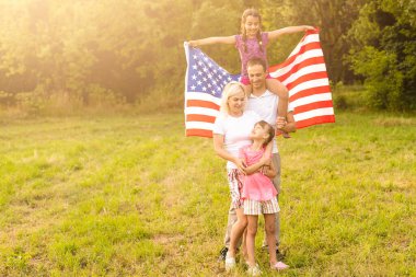 Amerikan bayrağı taşıyan ebeveynler ve çocuklar renkli bir uçurtmayla oynuyorlar. Anne, baba ve küçük kızları sisli bir günde 4 Temmuz 'u birlikte kutluyorlar. ABD 'nin Bağımsızlık Günü konsepti.