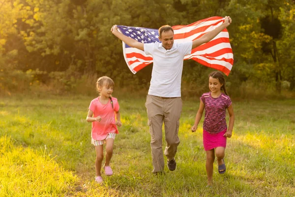 Vacaciones patrióticas. Familia feliz, madre e hijas con bandera americana al aire libre al atardecer. EE.UU. celebra el día de la independencia 4 de julio. — Foto de Stock