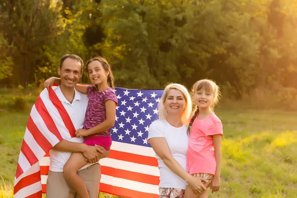 Padres y niños con bandera americana están jugando con una cometa de colores. madre, padre y sus hijas celebran juntos el 4 de julio al aire libre en un día de niebla. Concepto del Día de la Independencia de EE.UU.. — Foto de Stock