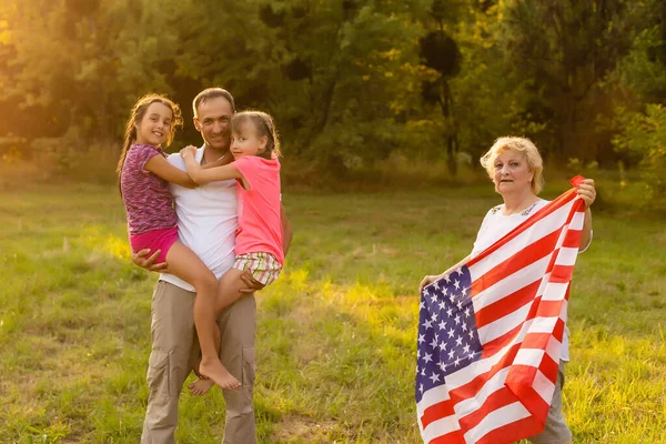 Padres y niños con bandera americana están jugando con una cometa de colores. madre, padre y sus hijas celebran juntos el 4 de julio al aire libre en un día de niebla. Concepto del Día de la Independencia de EE.UU.. — Foto de Stock