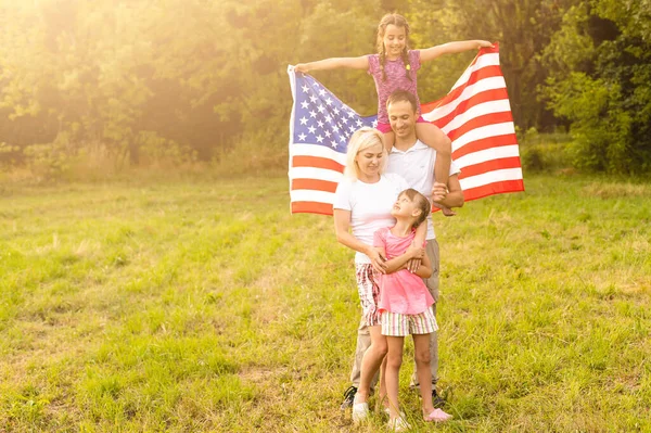 Parents and child with American flag are playing with a colorful kite. mother, father and their little daughters celebrate together 4th of July outdoors in foggy day. Independence Day of USA concept. — Stock Photo, Image