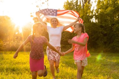 Amerikan bayrağı taşıyan ebeveynler ve çocuklar renkli bir uçurtmayla oynuyorlar. Anne, baba ve küçük kızları sisli bir günde 4 Temmuz 'u birlikte kutluyorlar. ABD 'nin Bağımsızlık Günü konsepti.