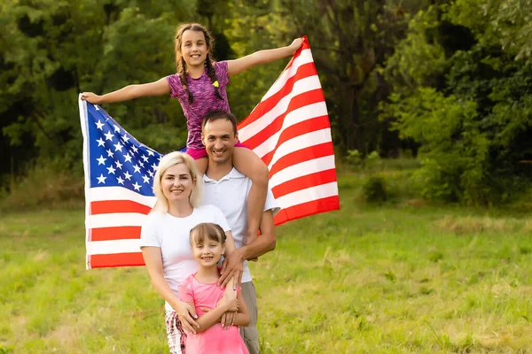 Familia feliz en el campo con EE.UU., bandera americana en la espalda. — Foto de Stock