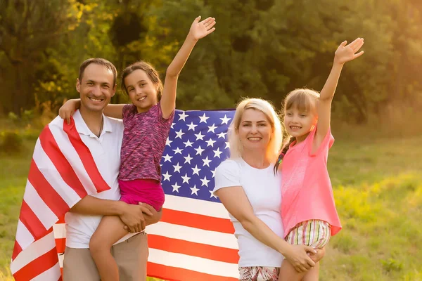 幸福的一家人坐在自家后院，身后举着美国国旗。笑着和孩子们一起举着美国国旗庆祝美国独立日 — 图库照片