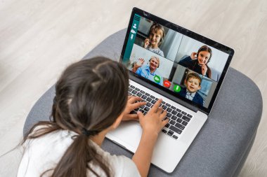 Genç bir kızın evde oturup konuşmasına, öğretmeniyle veya öğretmeniyle çevrimiçi video dersi almasına webcam sohbetine katılan genç bir kız çocuğuna, dizüstü bilgisayarında uzak kullanım konferansı uygulamasına çalışmasına.