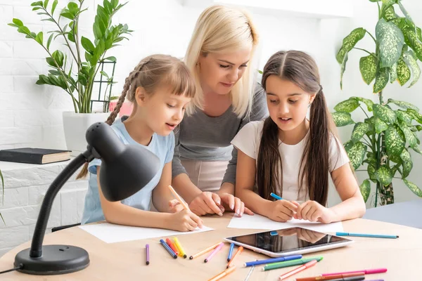 Hermosa madre joven ayudando a sus hijas con la tarea. — Foto de Stock