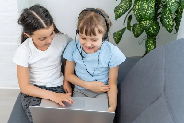 Foto di ragazze serie con cuffie digitando con la sua amica vicino al computer portatile, online — Foto Stock