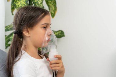 Hasta küçük kız, gri arka planda fotokopi çekerek nefes alıyor. Evde nebulizörle solunum yapan bir kız. çocuk astım spreyi soluması nebulizer buhar tutması öksürüğü