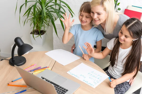 Una tutor donna o madre adottiva che aiuta la ragazza caucasica carina della scuola a fare i compiti a tavola. Diverse bambinaia e bambino imparare a scrivere in notebook studiare a casa — Foto Stock