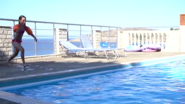 Vacker liten flicka hoppar i poolen mot havet — Stockvideo