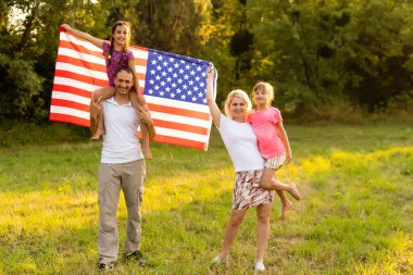 Gün batımında buğday tarlasında Amerikan bayrağı taşıyan mutlu bir aile. Bağımsızlık Günü, 4 Temmuz.