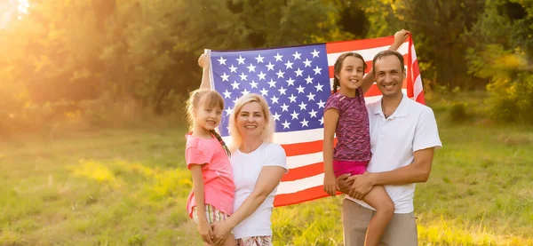 Happy family with the flag of america USA at sunset outdoors — Stock Photo, Image