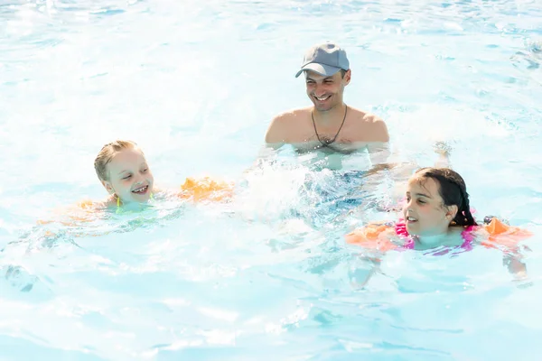 Aktif bir baba çocuklarına tropik tatil köyünde havuzda yüzmeyi öğretiyor. Yaz tatilleri ve spor konsepti — Stok fotoğraf