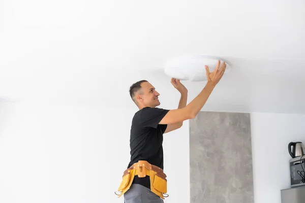 Worker repairing lamp on stretch ceiling indoors — Stock Photo, Image