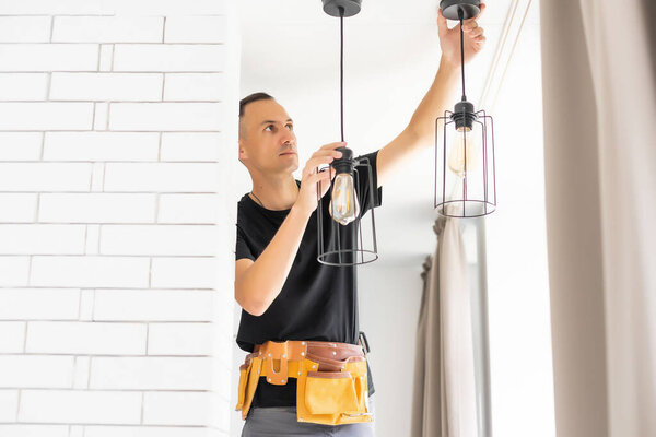 Worker repairing lamp on stretch ceiling indoors