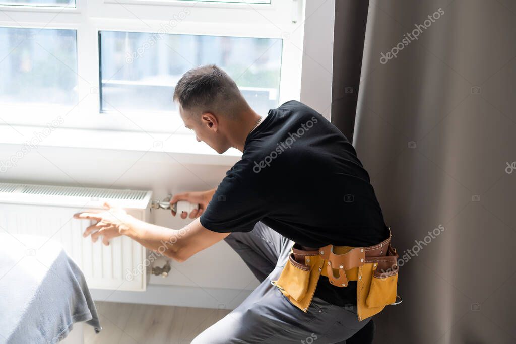 young man plumber checking radiator while installing heating system in apartment