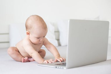 Beyaz yatakta dizüstü bilgisayarı olan şirin bir bebek.