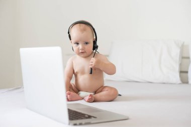 Beyaz yatakta dizüstü bilgisayarı olan şirin bir bebek.