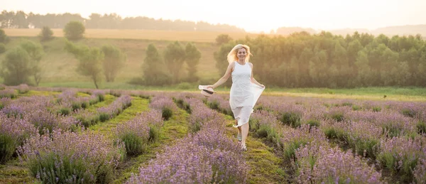Gyönyörű fiatal nő, fehér ruhában sétál a levendulamezőn, virágban. — Stock Fotó