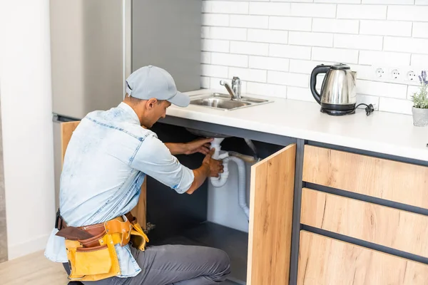 plumber fixes sink siphon by two pipe-wrenches in kitchen.