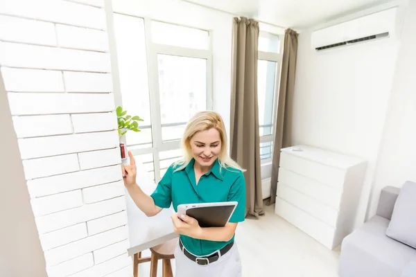 Mujer que regula la temperatura de calefacción con un termostato inalámbrico moderno instalado en la pared blanca en casa. Concepto de regulación inteligente de calefacción doméstica — Foto de Stock