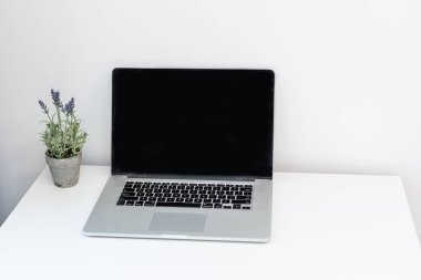 Beyaz duvar arka planlı beyaz masadaki boş ekran laptopuyla modern çalışma alanının kırpılmış görüntüsü
