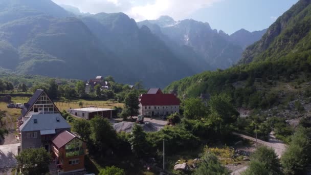 Vliegen in de buurt van oude houten kerk en bomen in Thethi vallei, Albanië. Luchtfoto van Theth National Park, Albanese Alpen. Dorp, rivier en rotsachtige bergen op de achtergrond. — Stockvideo