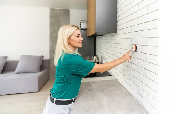 Mujer que regula la temperatura de calefacción con un termostato inalámbrico moderno instalado en la pared blanca en casa. Concepto de regulación inteligente de calefacción doméstica — Foto de Stock