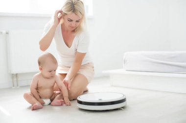 Toddler robot elektrik süpürgesinin yanında oturuyor. Yukarıdan bak. Ev işi. Alerji kontrolü