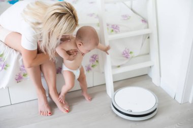 Toddler robot elektrik süpürgesinin yanında oturuyor. Yukarıdan bak. Ev işi. Alerji kontrolü