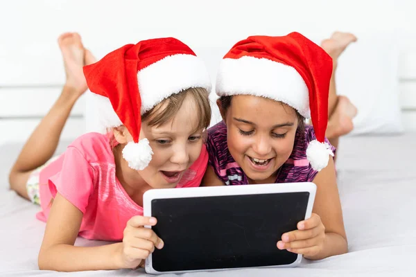 Noel, Noel, Noel, kış, mutluluk konsepti - tabletle oynayan iki sevimli kıvırcık kız — Stok fotoğraf