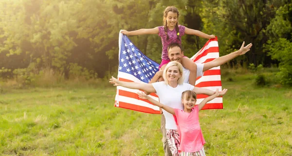 Happy family with the flag of america USA at sunset outdoors — Stock Photo, Image