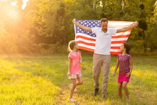 Vacaciones patrióticas. Familia feliz, madre e hijas con bandera americana al aire libre al atardecer. EE.UU. celebra el día de la independencia 4 de julio. — Foto de Stock