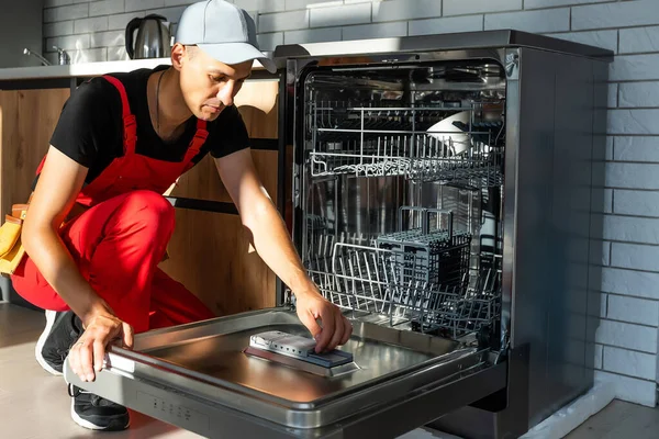 若い修理工サービスキッチンで食器洗い機のアプライアンスを修復します — ストック写真