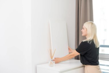 Beyaz tuval, arka planda gri duvar olan kadınların elinde. Duvarda boş resimli bir resim asılı duran bir kadın. Duvar dekoru. Çerçeveye gerilmiş tuval.