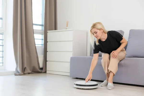 Mladá žena pomocí automatického vysavače čistit podlahu, ovládání stroje domácí práce robot — Stock fotografie