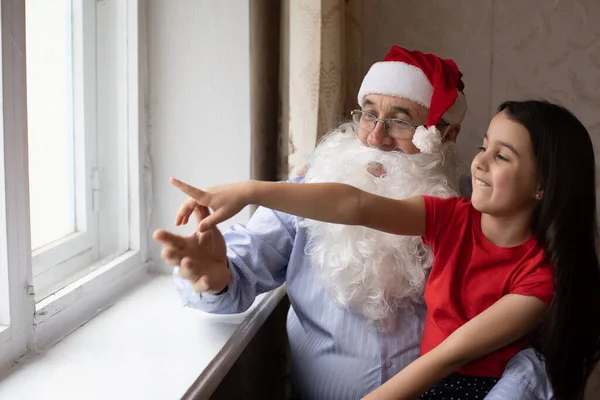 Egy idős férfi télapó kalapban és egy unokával. — Stock Fotó